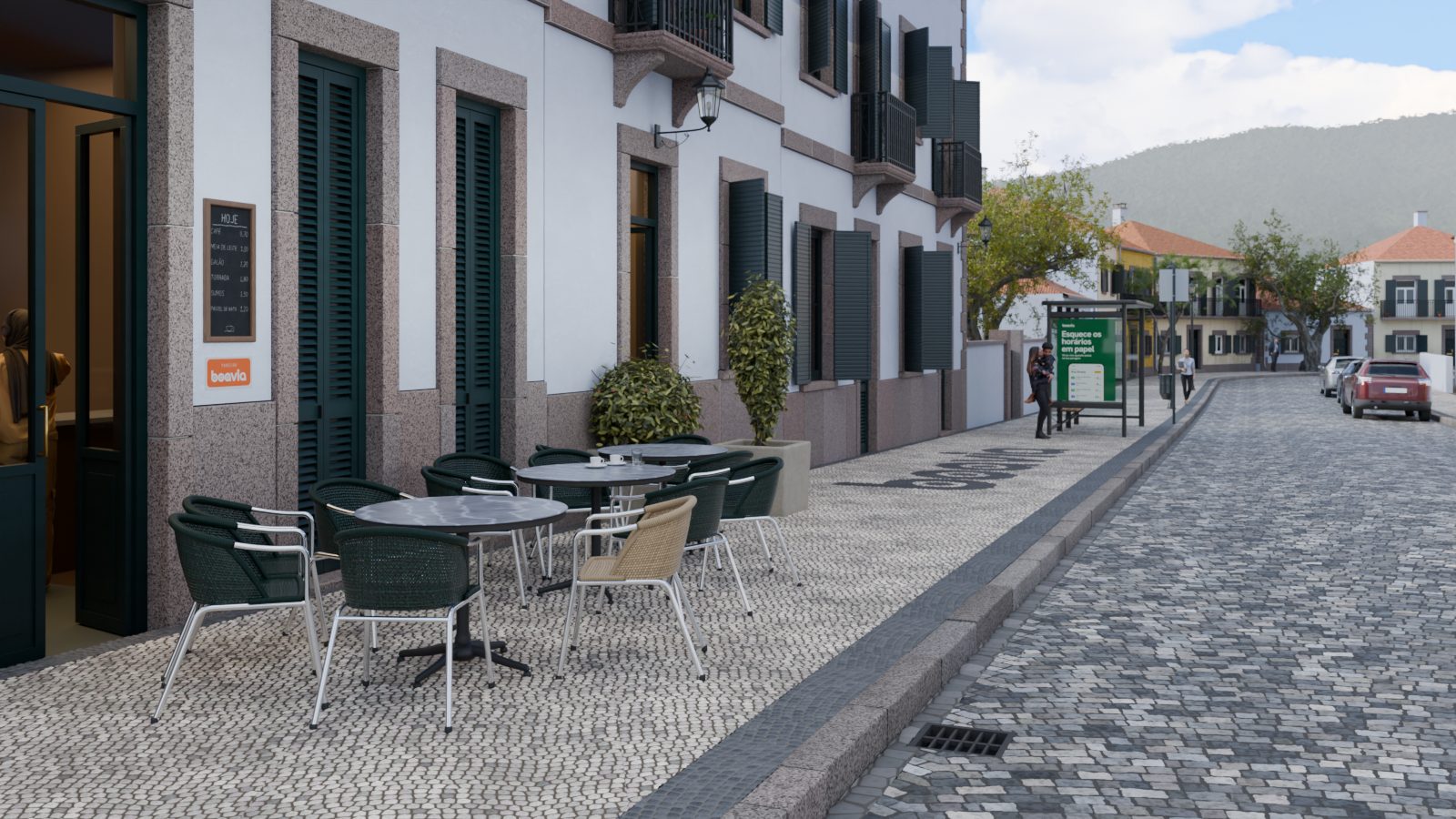Rua estreita de manhã, com mesas de esplanada na calçada e um abrigo de paragem ao fundo.